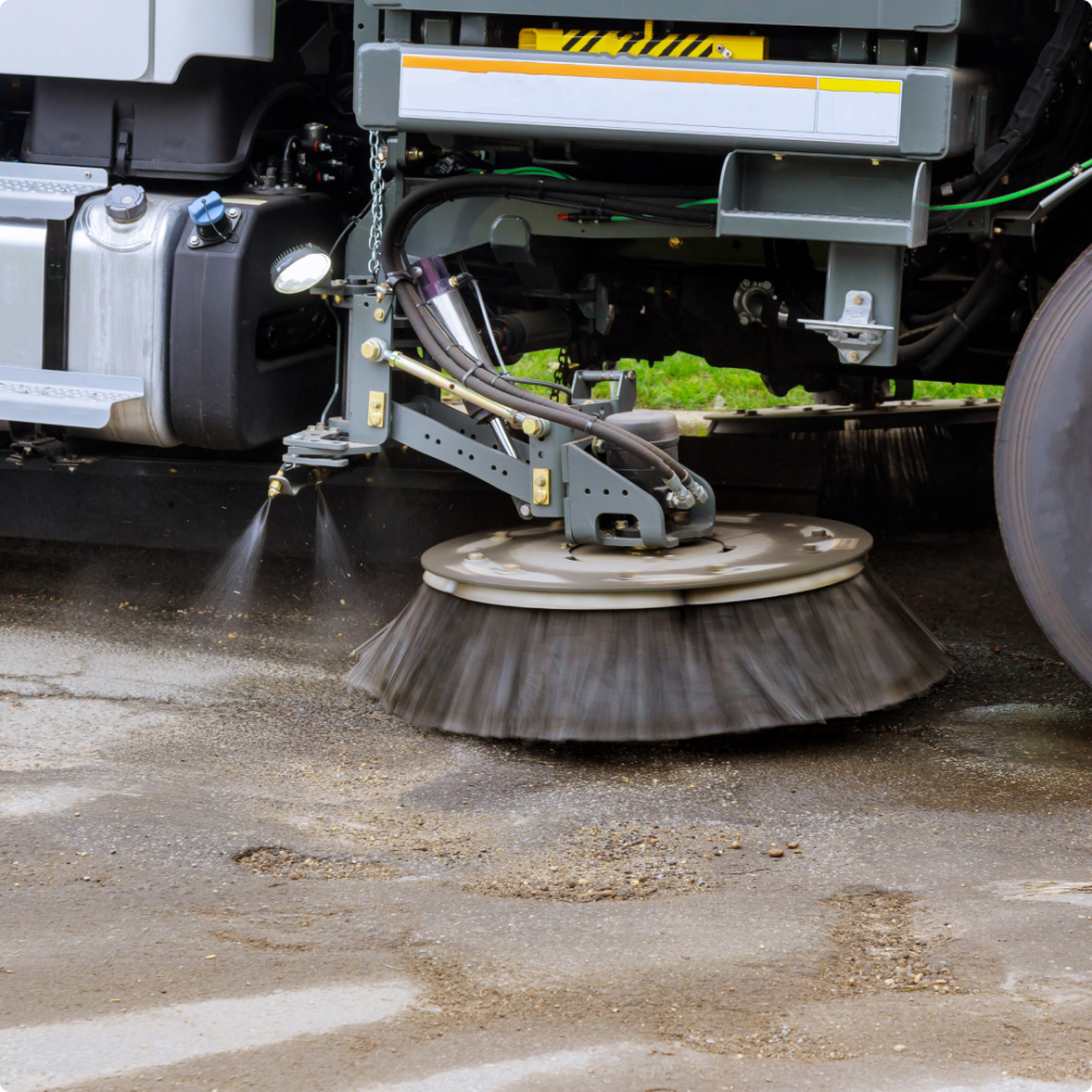 A street sweeper with a large circular brush cleaning the pavement.