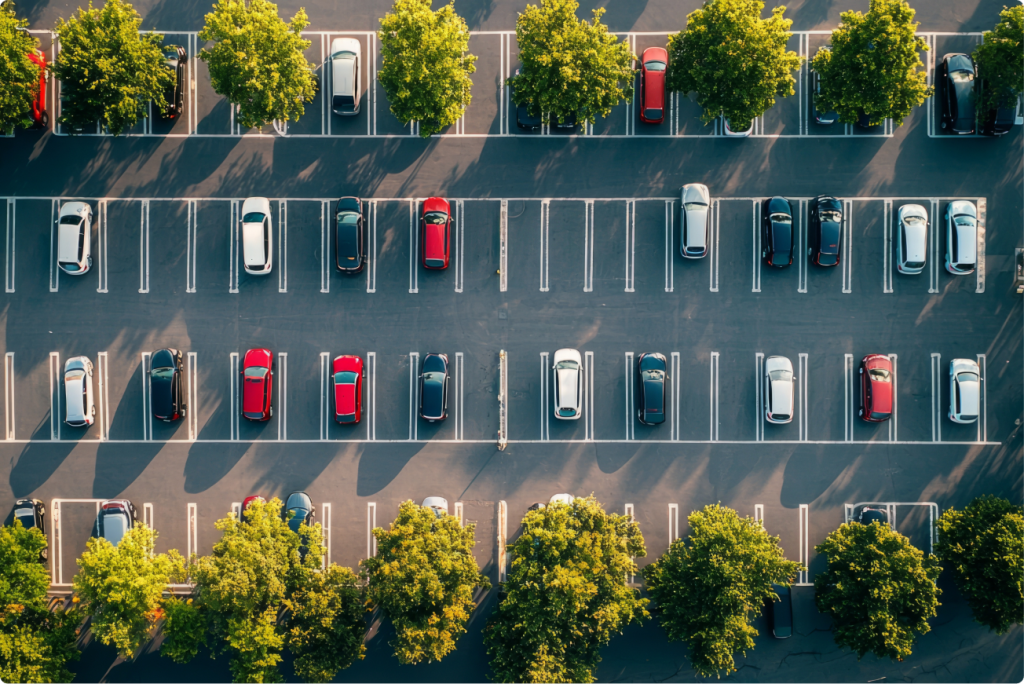 Aerial view of a parking lot with rows of parked cars and trees lining the edges.
