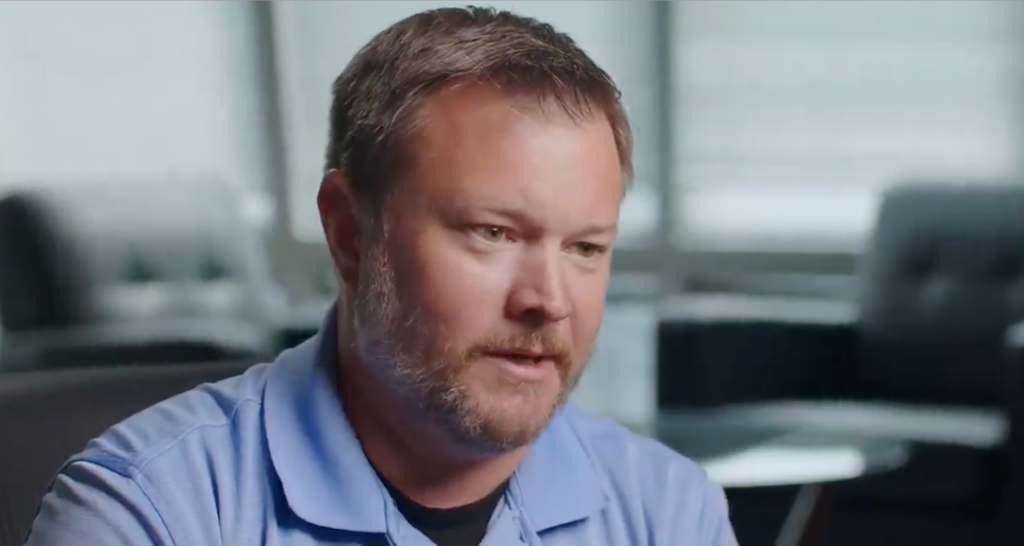 Man wearing a blue polo shirt sits in an office.