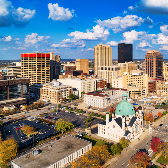 City skyline with a turquoise-domed church in the foreground beneath a bright blue, partly cloudy sky.